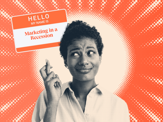 a hubspot-branded featured image of a woman crossing her fingers while looking up at a nametag that says ‘marketing in a recession’